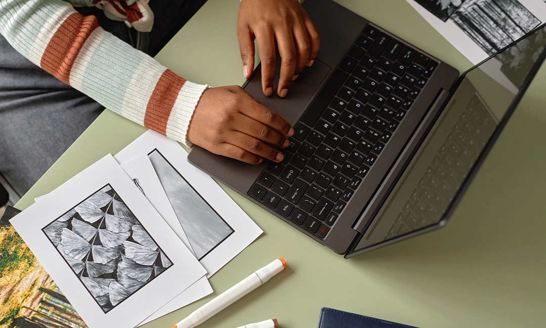 Person working on laptop with printed PDF documents next to them