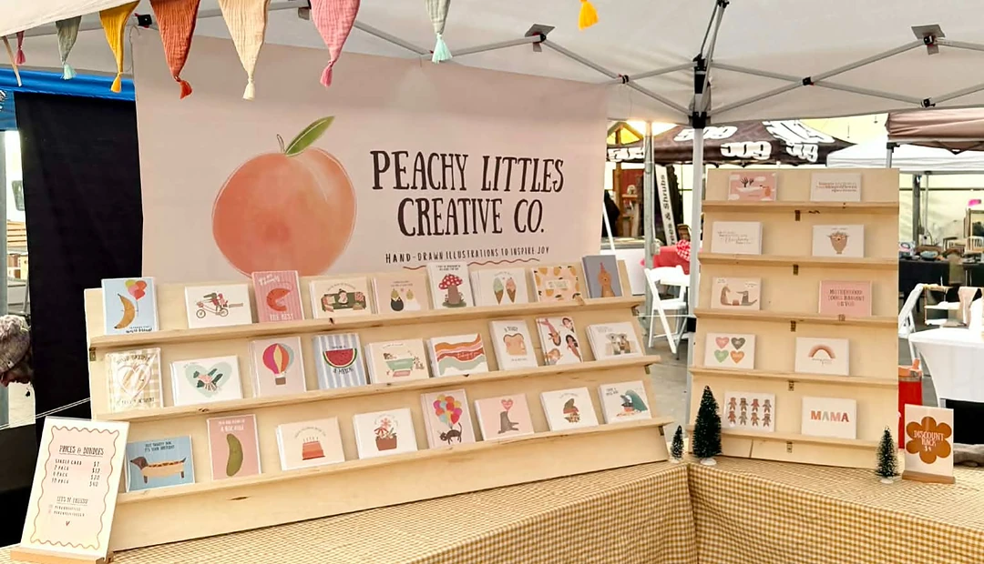 Peachy Littles Creative Co. market display featuring illustrated greeting cards printed at Little Rock Printing.